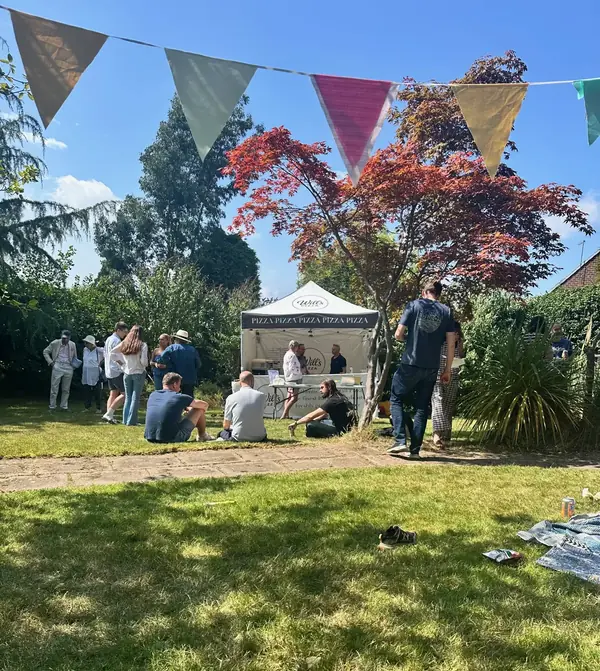 A summer garden party under bunting, with guests on the lawn and the Will's Pizza gazebo serving fresh pizza