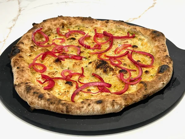 A roast garlic and three cheese pizza, golden and blistered, topped with pickled red onion