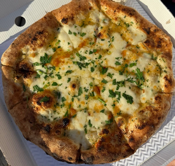 A roast garlic and three cheese pizza in an open box, golden and blistered, scattered with fresh parsley